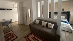 A modern living room with a sofa, a dining table, and a kitchen area visible through a partition.
