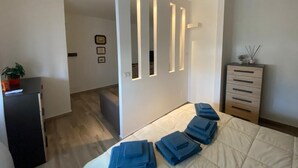A modern bedroom with a bed, bedside tables, a dresser, and a wall with built-in lighting.