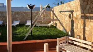 An outdoor patio area with a stone wall, a wooden pergola, and a wooden bench.