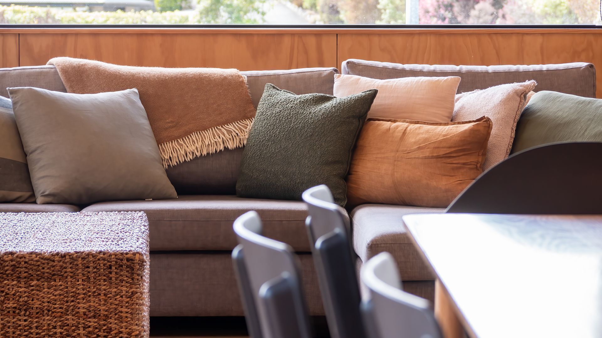 A modern living room with a brown sofa, multiple cushions, and a view of greenery outside.