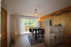 Una habitación con pared de madera, una mesa de comedor con sillas, un ventanal con vistas a la vegetación y una lámpara en el techo.