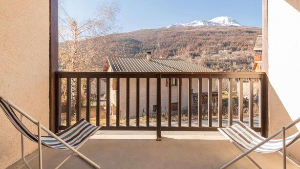 Un balcon avec deux chaises à rayures, une rambarde en métal et une vue sur une montagne dont les sommets sont enneigés.