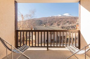 A balcony with two striped chairs, a metal railing, and a view of a mountain with snow-capped peaks. - 1st floor, view mountain, balcony, tv, 30m², Serre Chevalier (Briançon)
