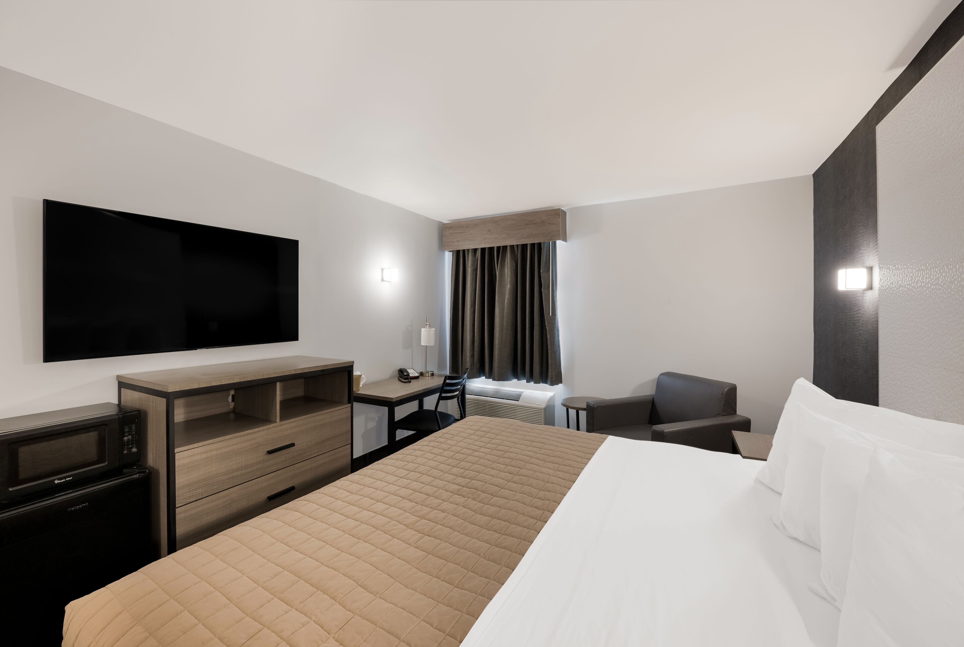 Habitación de hotel con una cama grande, un escritorio con silla, televisor de pantalla plana en la pared y una ventana con cortinas.