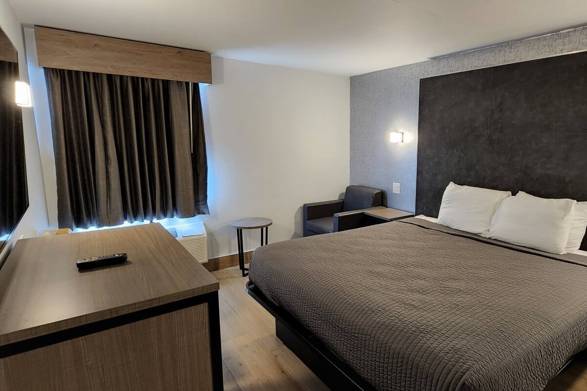 A modern hotel room with a large bed, a desk, a chair, and a TV.