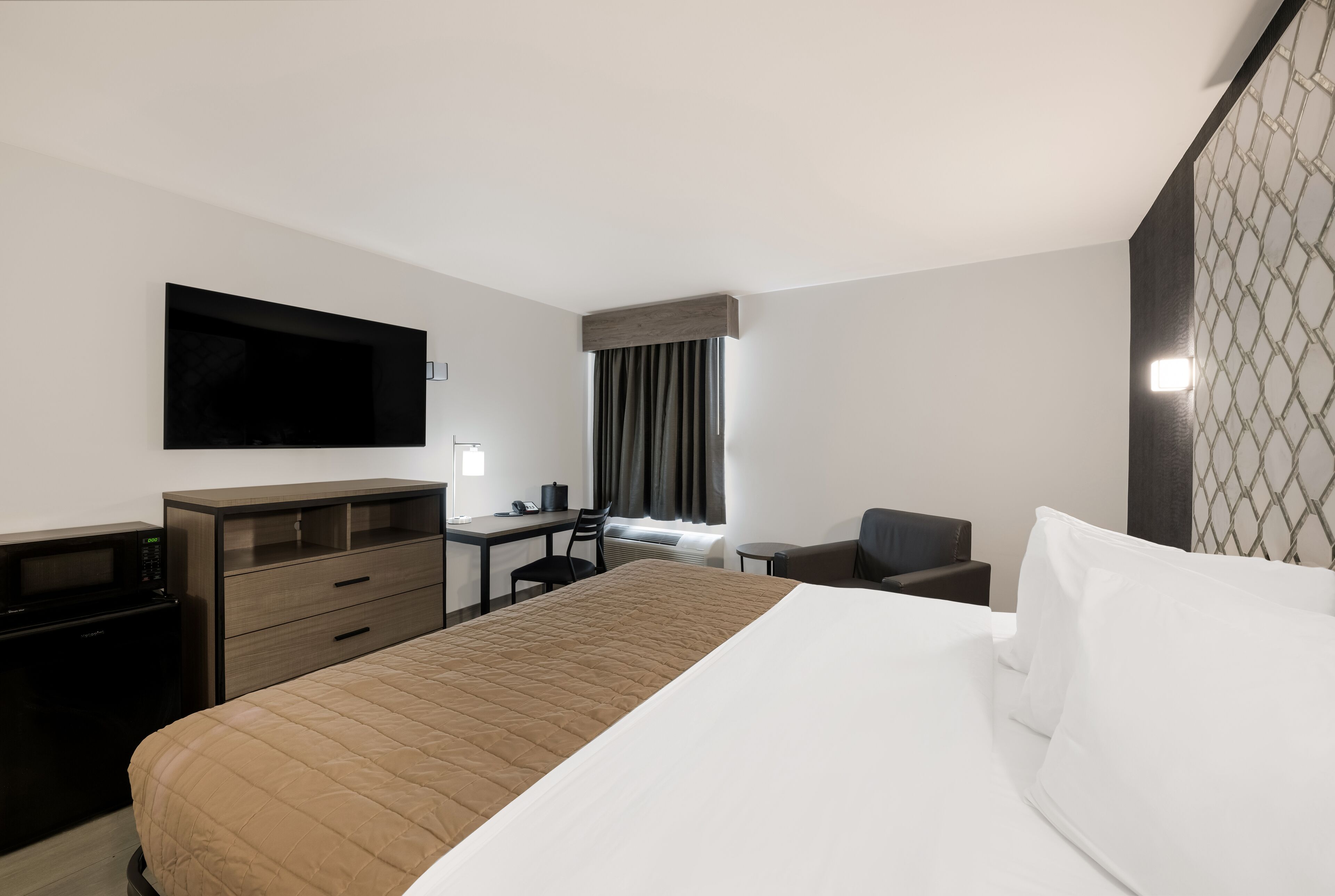 Hotellihuone, jossa on sänky, työpöytä, tuoli, televisio ja mikroaaltouuni.