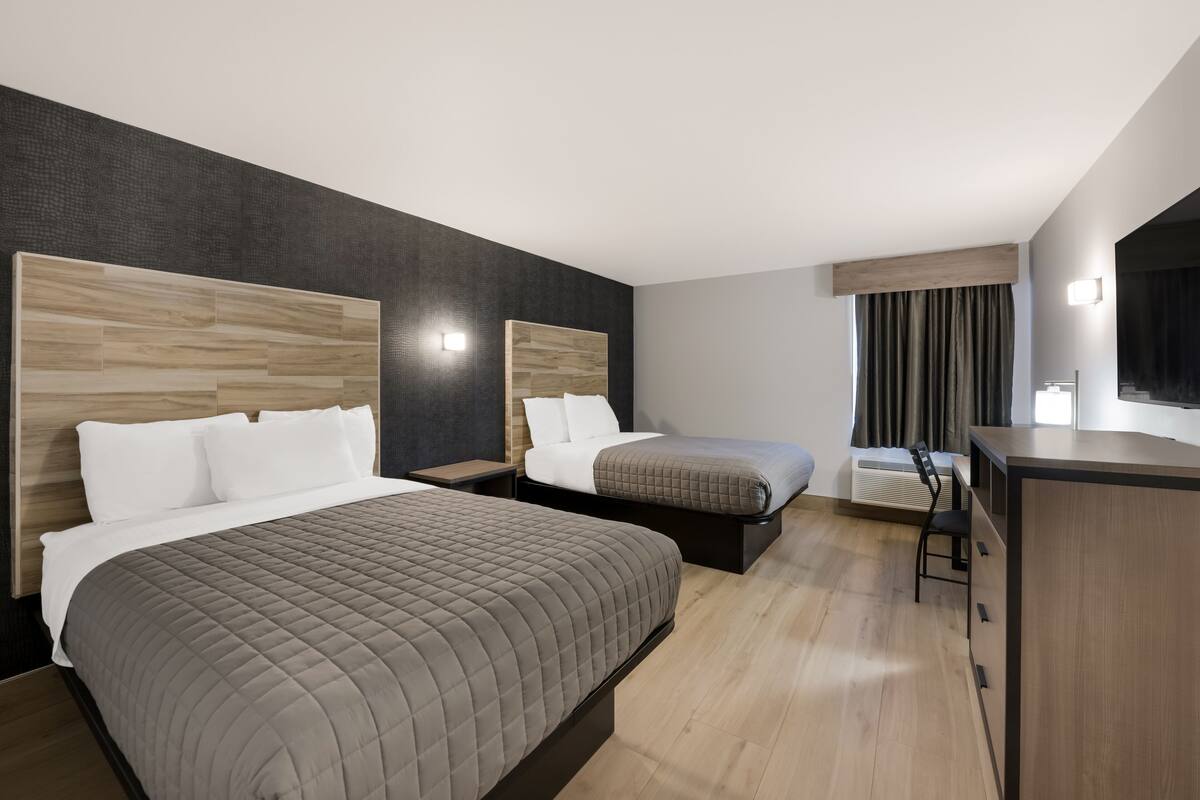 A hotel room with two beds, a desk, and a chair.