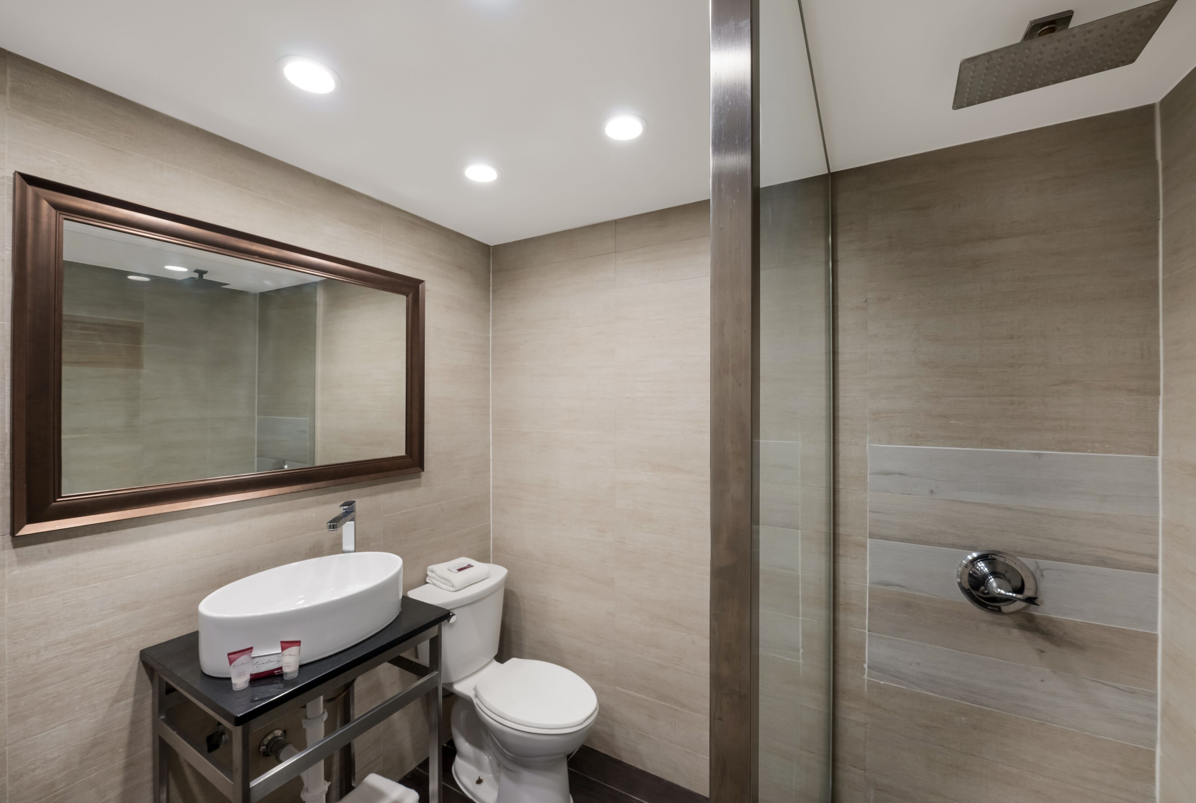 Un baño moderno con un espejo grande, un lavamanos, un inodoro y una zona de ducha.