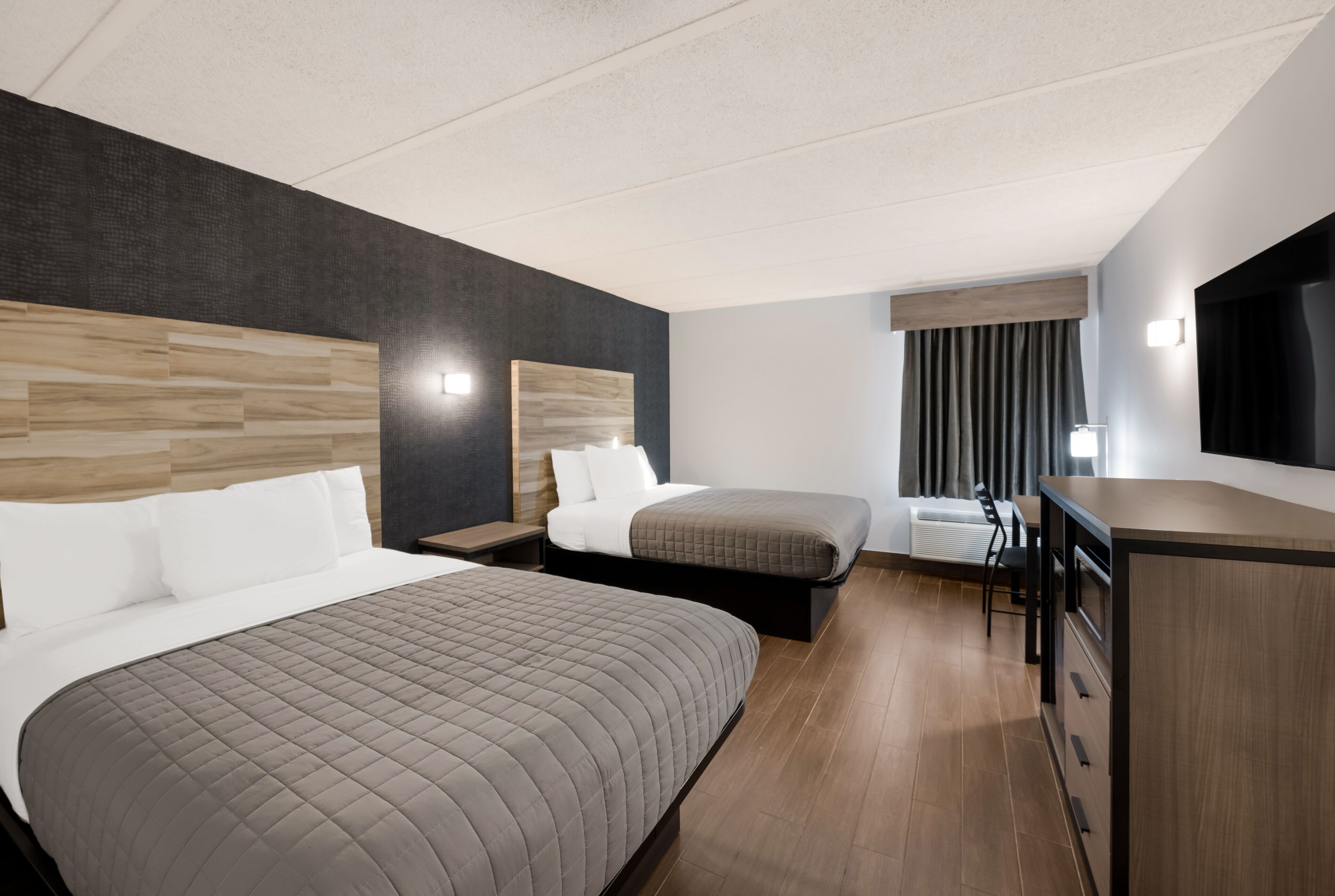 A hotel room with two beds, a desk, and a chair.