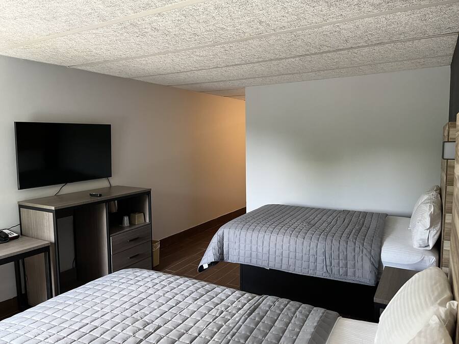 A hotel room with a flat-screen TV, a desk with a chair, and two beds with grey bedding.