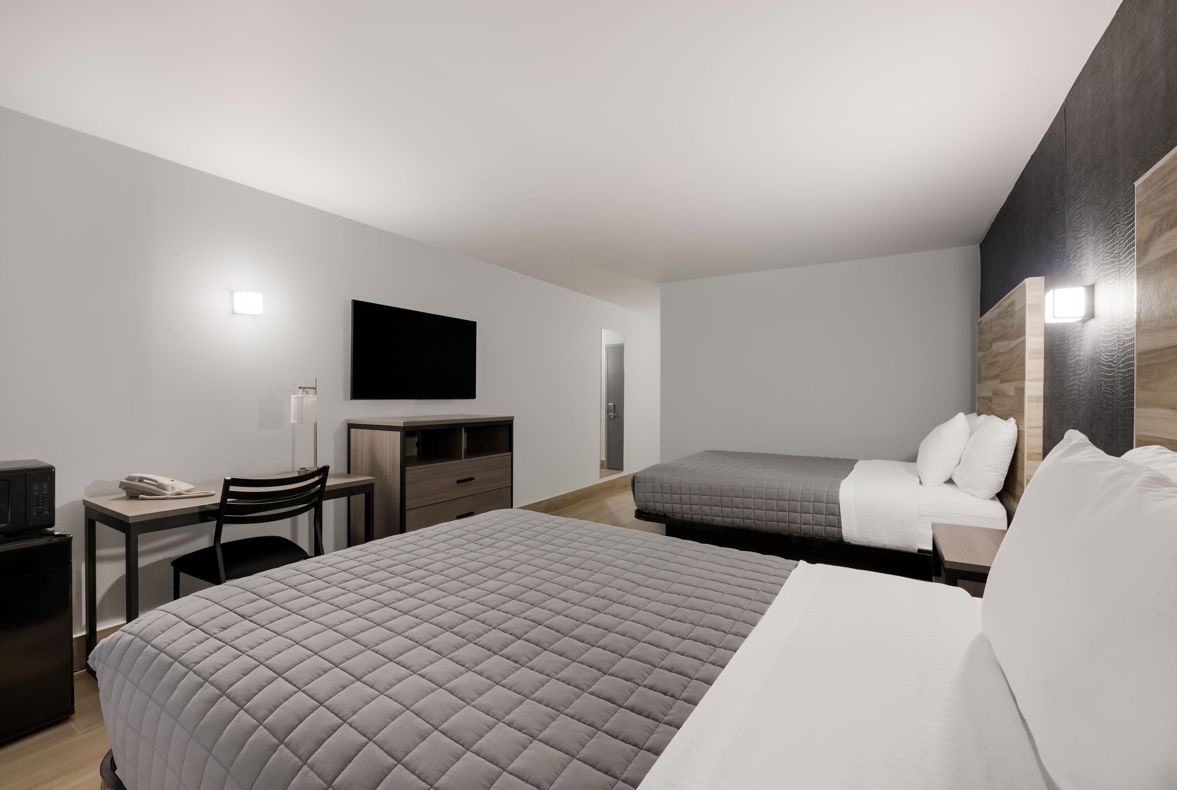 A modern hotel room with a large bed, a desk with a chair, a flat-screen TV, and a small kitchenette.