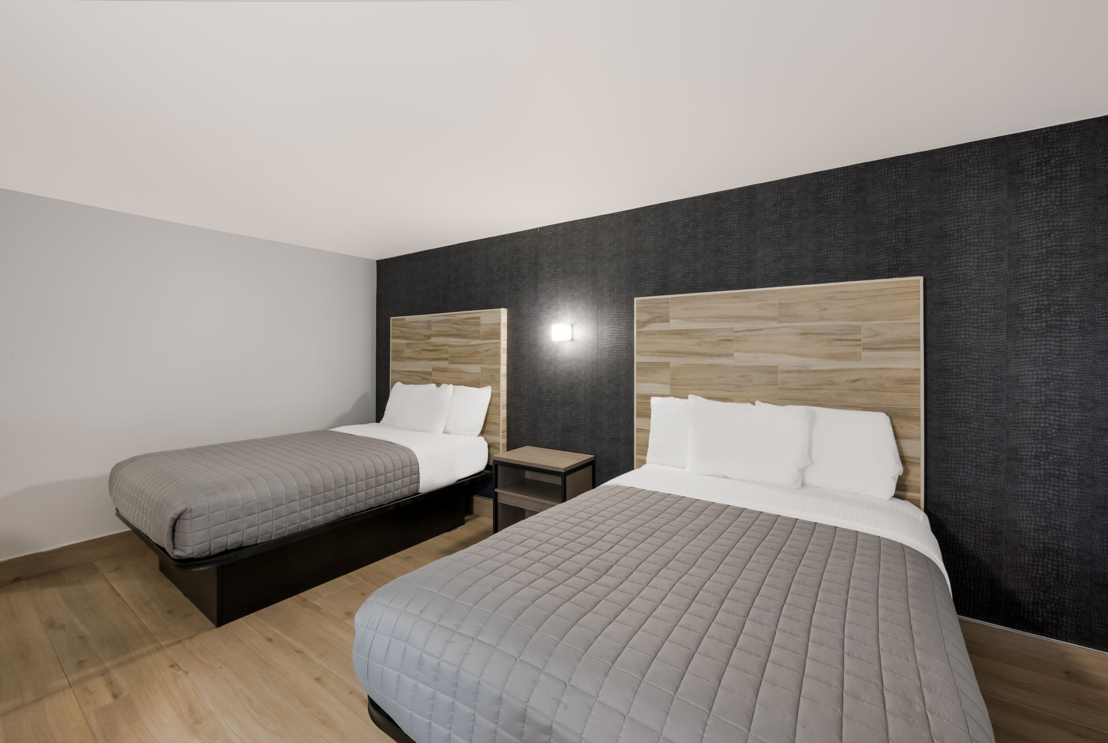 A hotel room with two beds, a nightstand, and a wall-mounted light.