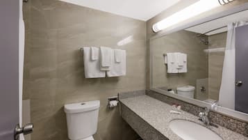 Une salle de bain moderne avec un mur en marbre, des toilettes blanches, un comptoir en granit, un lavabo et un grand miroir.