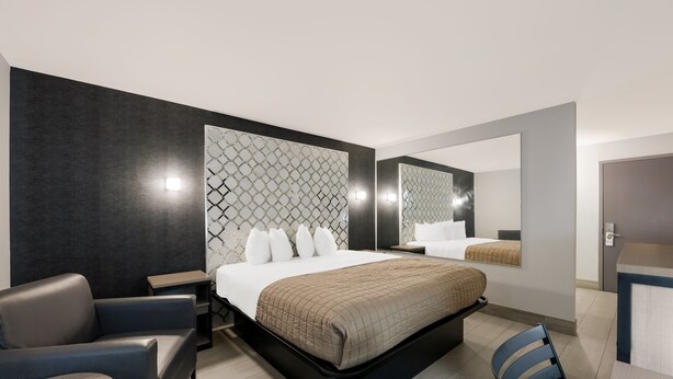 A modern hotel room with a large bed, a seating area with a chair and table, a mirror, and a small desk.