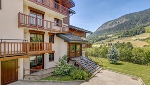 A multi-story building with wooden balconies, a staircase leading to the entrance, and a view of a mountainous landscape.