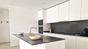 A modern kitchen with white cabinets, a black countertop, and a central island with a bowl and faucet. - AL BORADA HOMES 3-Bedroom Apartment with Terrace in a Premium Residential Complex in Marbella (Benahavís)
