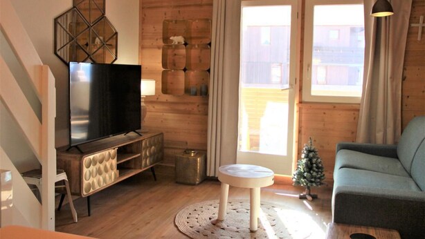 Un salon chaleureux avec un téléviseur, des murs en bois, un petit sapin de Noël et un canapé.