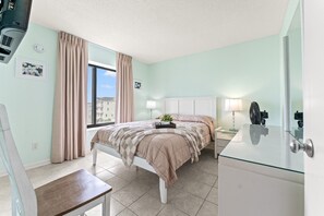 A bedroom with a bed, bedside table, lamp, and a window with curtains.
