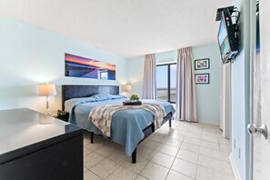 A hotel room with a bed, bedside lamps, a flat-screen TV, a window with curtains, and a wall-mounted picture.