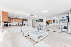 Een moderne woonkamer met een witte bank, een glazen salontafel en een eethoek met witte stoelen.