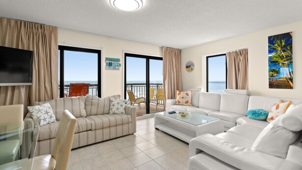 A modern living room with a sofa, armchairs, and a coffee table. There is a television mounted on the wall and a window with curtains. - Buena Vista 508-Oceanfront 3BR-Walk to Pier- Pool (North Myrtle Beach)