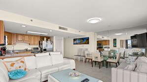 A modern living room with a white sofa, a glass coffee table, and a dining area with a glass table and chairs. - Buena Vista 508-Oceanfront 3BR-Walk to Pier- Pool (North Myrtle Beach)