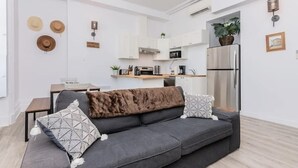 A modern living room with a grey sofa, a coffee table, and a kitchen area in the background. - Manoir des Remparts 3 Bdrm Oasis (Québec City)