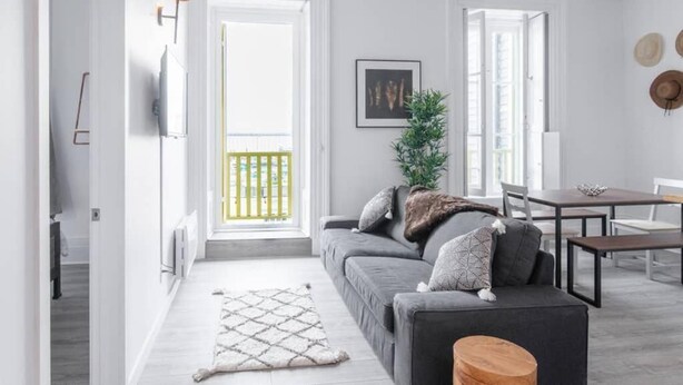 A modern living room with a grey sofa, a wooden coffee table, and a dining area with a table and chairs. - Manoir des Remparts 3 Bdrm Oasis (Québec City)