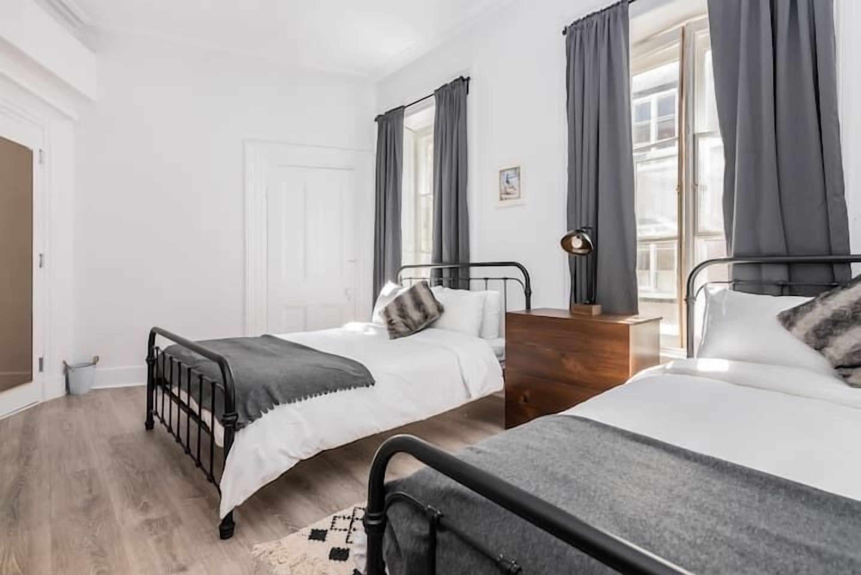 A bedroom with two beds, a wooden dresser, and a window with curtains.