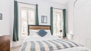 A neatly arranged bedroom with a large bed, a wooden dresser, and a window with curtains. - Manoir des Remparts 3 Bdrm Oasis (Québec City)