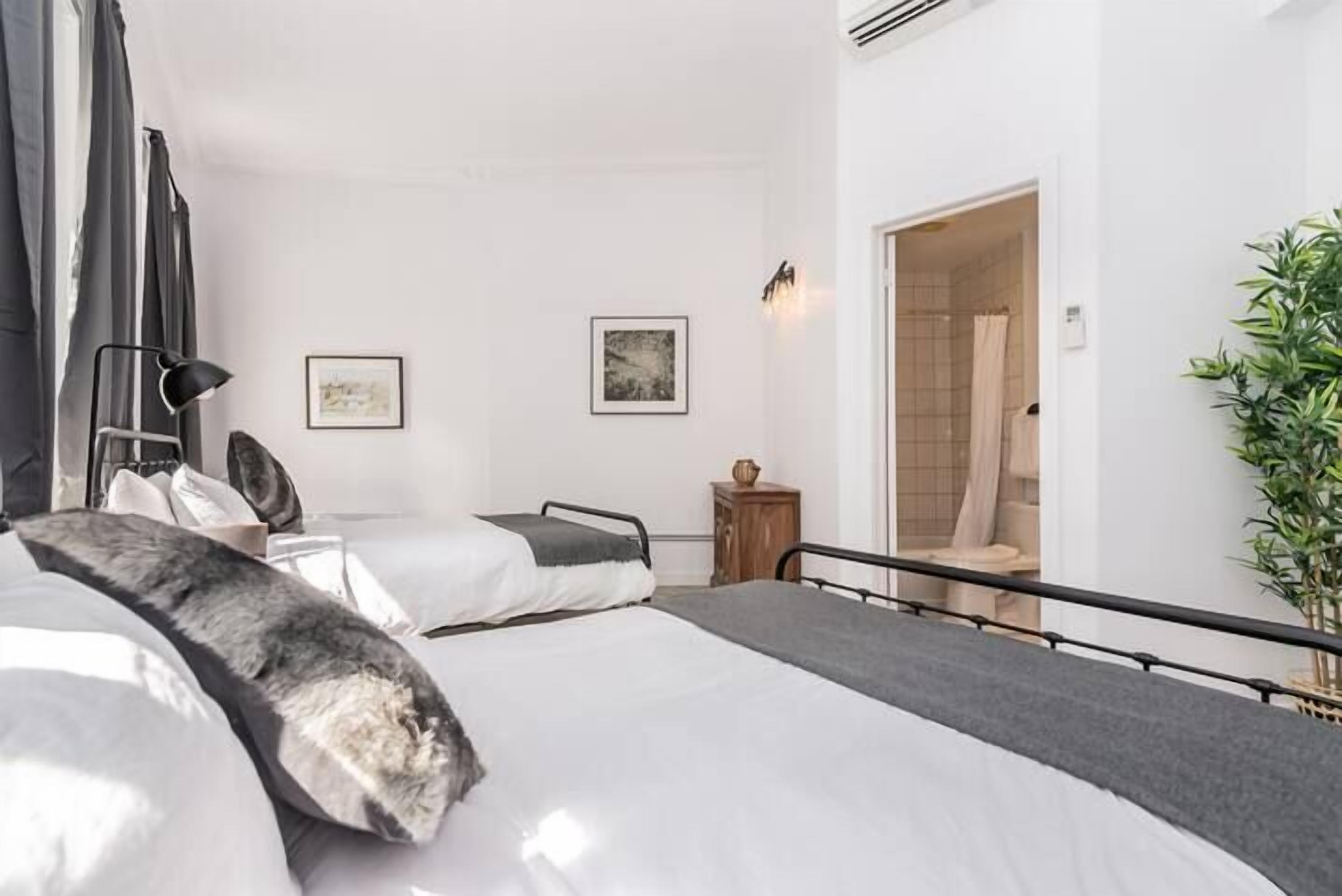 A hotel room with two beds, a wooden nightstand, a wall-mounted lamp, and a framed picture.