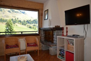 Enjoy a scenic view of rolling hills and a golf course from the comfort of this living room, featuring a fireplace, two comfortable chairs, and a flat-screen TV.
