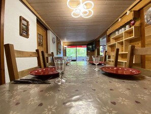 Uma sala de jantar com mesa posta para quatro pessoas, cadeiras de madeira e uma televisão na parede.