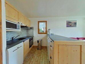 A compact kitchen with wooden cabinets, a built-in oven, a sink, and a window with a view.