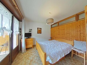 A bedroom with a wooden bed, a television on a wooden dresser, and a window with curtains.