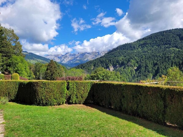 A landscaped garden with neatly trimmed hedges, a clear sky, and a mountain range in the background.