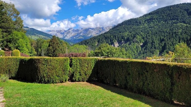 Un jardín ajardinado con setos podados y un cielo despejado, con una cadena montañosa al fondo.