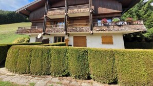 Un chalet de dos pisos con balcón, rodeado de setos cuidados y cielo despejado.