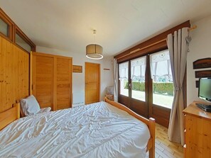 A bedroom with a large bed, wooden wardrobe, a television, and a window with curtains.