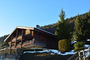 A wooden chalet with a balcony, surrounded by snow and trees.