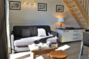 Ein modernes Wohnzimmer mit einer Couch, einem Holztisch mit Teekanne, einer Lampe und einer Treppe zu einer Küchenzeile.