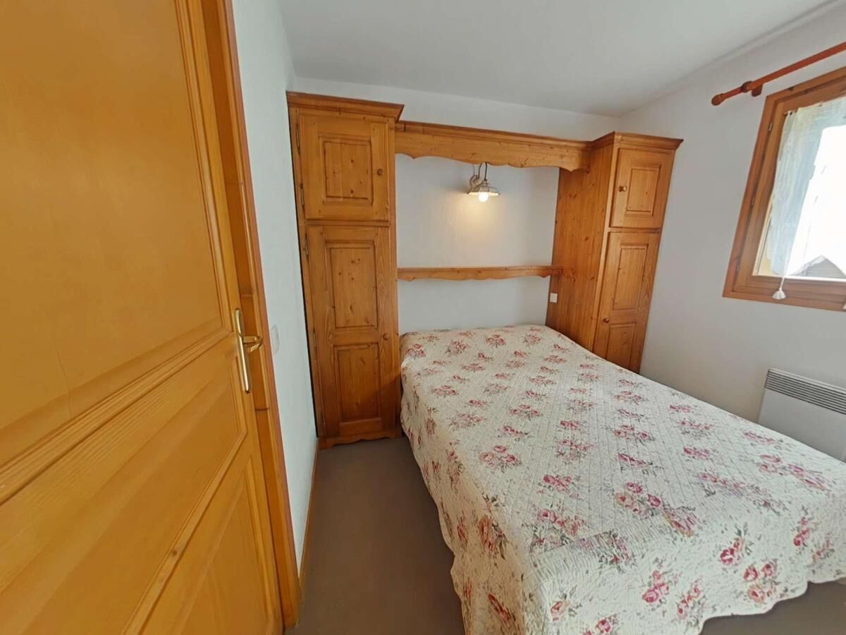A bedroom with a bed, wooden wardrobe, and a window.