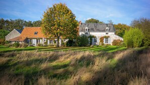 Ein großes, zweistöckiges Haus mit einem geneigten Dach, umgeben von einer Wiese und Bäumen.