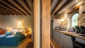 Ein Schlafzimmer mit Bett, Nachttisch, Lampe und Blick zur Küche.