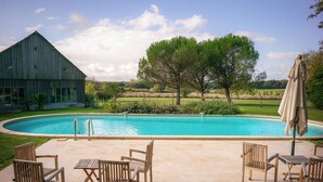 Ein Pool mit Holzstühlen und -tischen, ein Bauernhof und ein Baum im Hintergrund.