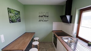 A compact kitchen with a wooden countertop, three stools, a stainless steel sink, and a wall-mounted picture of plants.