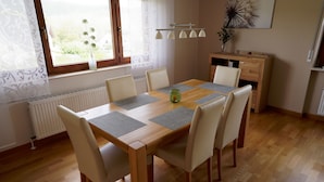 A dining room with a wooden table, six chairs, a radiator, a window with curtains, a cabinet, and a wall-mounted light fixture.