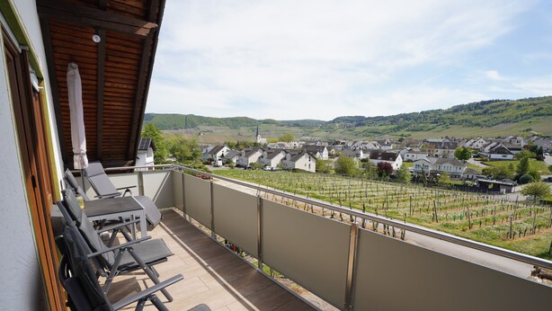 A balcony with sun loungers and a view of a vineyard and village.