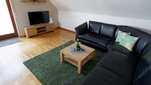 A living room with a black leather sofa, a wooden coffee table with a plant, and a TV on a wooden stand.