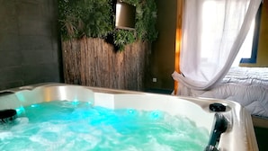 Een bubbelbad met blauwe verlichting, een houten wand met beplanting, en een bed met witte gordijnen.